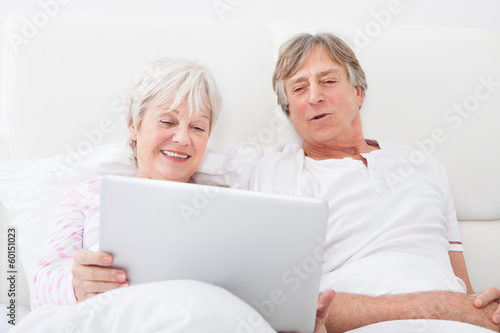 Photo: Senior Couple On Bed Looking At Laptop Senior Couple On Bed Looking At Laptop