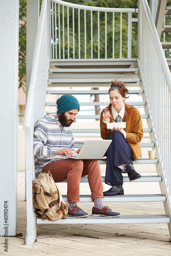 Photo: Hipster couple using computer and eating lunch outdoors Hipster couple using computer and eating lunch outdoors