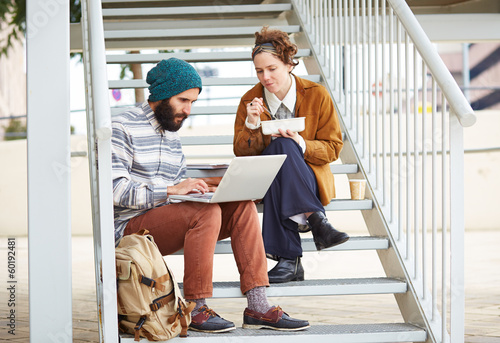 Photo: Hipster couple using computer and eating lunch outdoors Hipster couple using computer and eating lunch outdoors