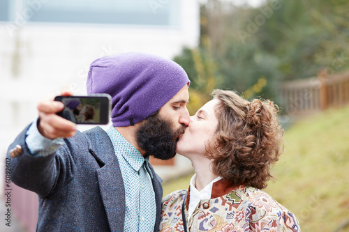 Photo: Couple taking a photograph of themselves kissing with a smartpho Couple taking a photograph of themselves kissing with a smartpho