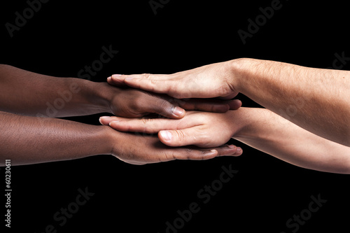 Photo: Multiracial hands together forming a pile over dark background Multiracial hands together forming a pile over dark background