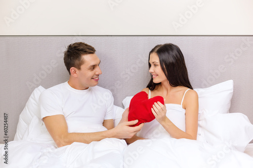 Photo: smiling couple in bed with red heart shape pillow smiling couple in bed with red heart shape pillow