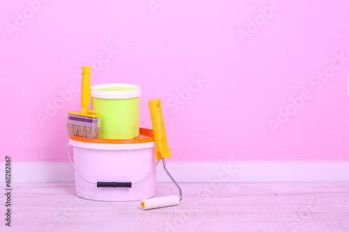 Photo: Paints, roll and paintbrush on floor in room on wall background Paints, roll and paintbrush on floor in room on wall background