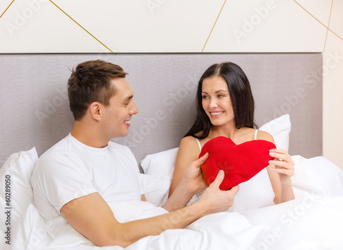 Photo: smiling couple in bed with red heart shape pillow smiling couple in bed with red heart shape pillow
