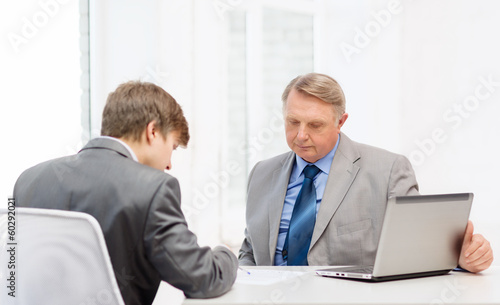 Photo: older man and young man signing papers in office older man and young man signing papers in office