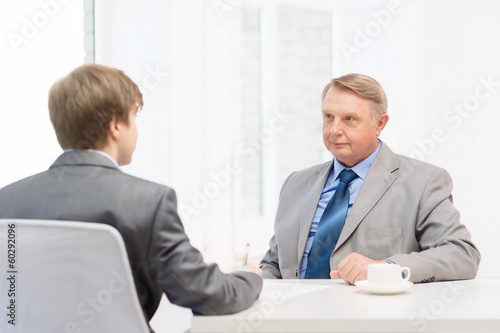 Photo: older man and young man signing papers in office older man and young man signing papers in office