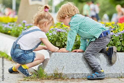Photo: Little boy and girl play at edge of flowerbed on square Little boy and girl play at edge of flowerbed on square