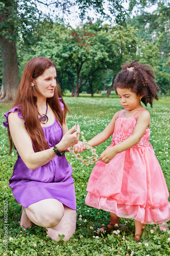 Photo: Mother stands on one knee on grass in park and gives flower Mother stands on one knee on grass in park and gives flower
