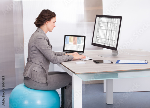 Photo: Woman Sitting On Pilates Ball Using Computer Woman Sitting On Pilates Ball Using Computer
