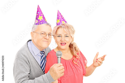 Photo: Middle aged couple with party hats singing on microphone Middle aged couple with party hats singing on microphone