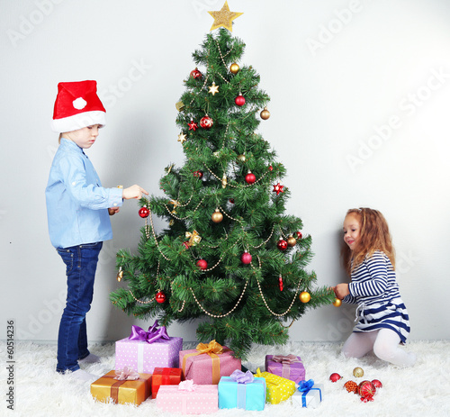 Photo: Kids decorating Christmas tree with baubles in room Kids decorating Christmas tree with baubles in room