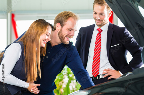 Photo: Young Couple and seller with auto in car dealership Young Couple and seller with auto in car dealership