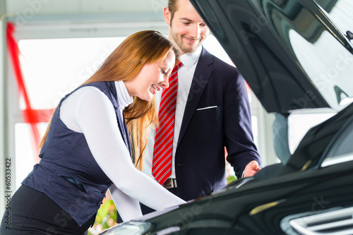 Photo: Young woman and seller with auto in car dealership Young woman and seller with auto in car dealership