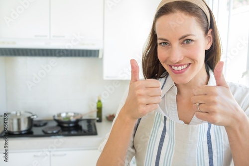 Photo: Smiling young woman gesturing thumbs up in kitchen Smiling young woman gesturing thumbs up in kitchen