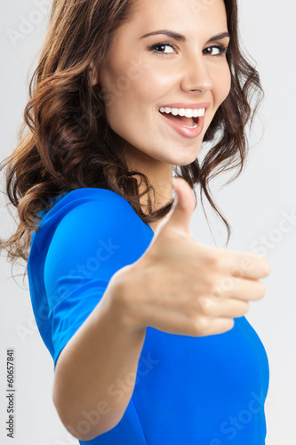Photo: Young woman with thumbs up gesture, over grey Young woman with thumbs up gesture, over grey