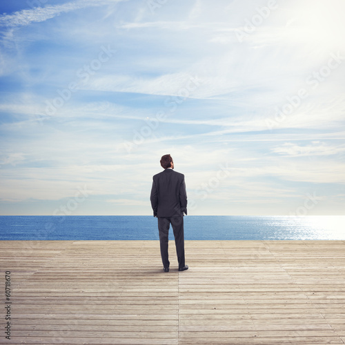 Photo: Business man standing on a pier looks the sea Business man standing on a pier looks the sea