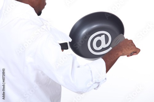 Photo: Afro-American chef drawing the at sign on a frying pan Afro-American chef drawing the at sign on a frying pan