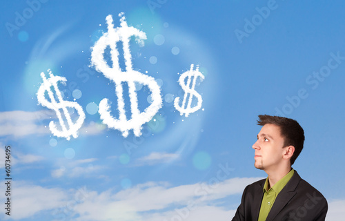 Photo: Businesman pointing at dollar sign clouds on blue sky Businesman pointing at dollar sign clouds on blue sky