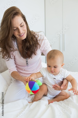 Photo: Mother and baby sitting with toy on bed Mother and baby sitting with toy on bed