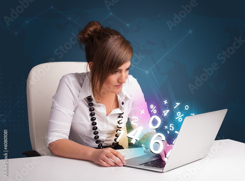 Photo: Beautiful young woman sitting at desk and typing on laptop with Beautiful young woman sitting at desk and typing on laptop with