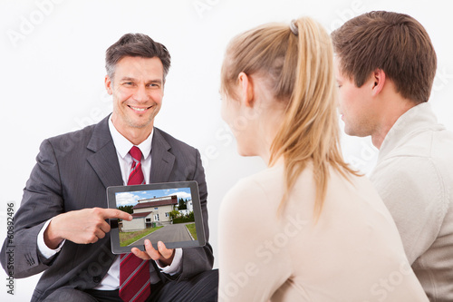 Photo: Agent With Tablet Pc Showing House To Couple Agent With Tablet Pc Showing House To Couple