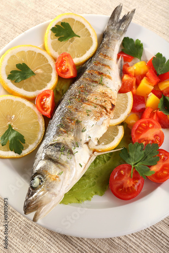 Photo: Delicious grilled fish on plate on table close-up Delicious grilled fish on plate on table close-up