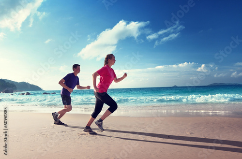 Photo: Man and women running on tropical beach at sunset Man and women running on tropical beach at sunset