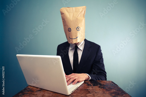 Photo: Businessman with bag over head working on computer Businessman with bag over head working on computer