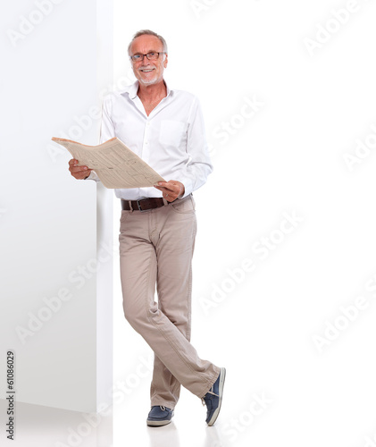Photo: Mature man with newspaper leaning against a wall Mature man with newspaper leaning against a wall