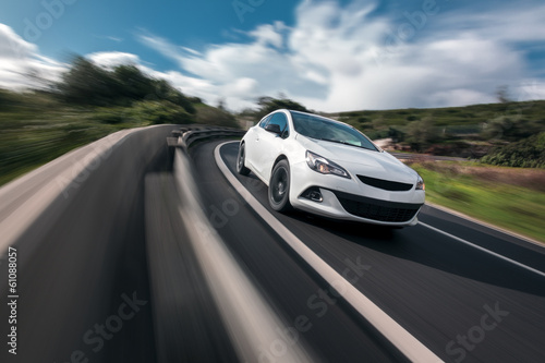 Photo: White car cornering in mountain road with speed blur White car cornering in mountain road with speed blur