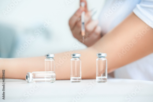 Photo: Closeup shot of ampules against patient doing injection Closeup shot of ampules against patient doing injection