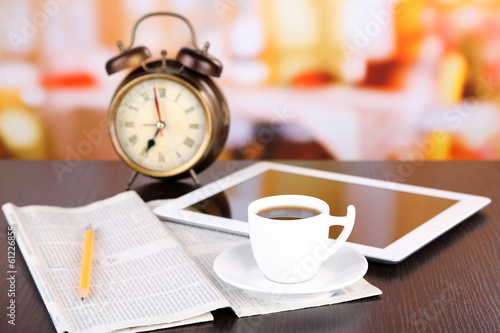 Photo: Tablet, newspaper, cup of coffee and alarm clock on wooden Tablet, newspaper, cup of coffee and alarm clock on wooden
