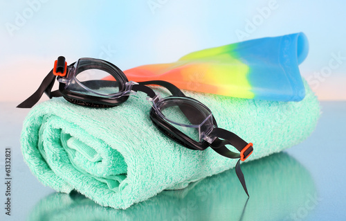 Photo: Set for pool: swim cap, goggles and towel on blue background Set for pool: swim cap, goggles and towel on blue background