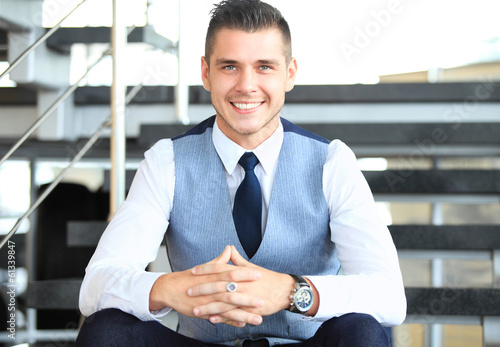 Photo: positive business man sitting on stairs of modern office positive business man sitting on stairs of modern office