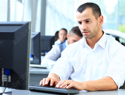 Photo: Casual businessman using laptop in office, sitting at desk Casual businessman using laptop in office, sitting at desk