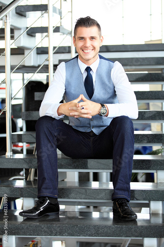 Photo: Positive business man sitting on stairs of modern office Positive business man sitting on stairs of modern office