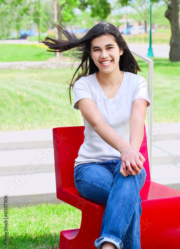Photo: Beautiful teen girl sitting outdoors on red chair Beautiful teen girl sitting outdoors on red chair