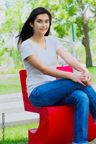 Photo: Beautiful teen girl sitting outdoors on red chair Beautiful teen girl sitting outdoors on red chair
