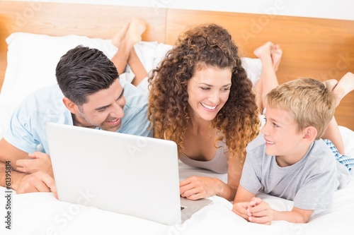 Photo: Smiling family using laptop together on bed Smiling family using laptop together on bed