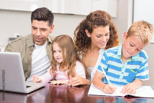 Photo: Cheerful parents colouring and using laptop with their children Cheerful parents colouring and using laptop with their children