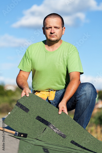 Photo: Worker holding bitumen roof shingles on top of building Worker holding bitumen roof shingles on top of building