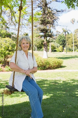 Photo: Smiling mature woman sitting on swing in park Smiling mature woman sitting on swing in park