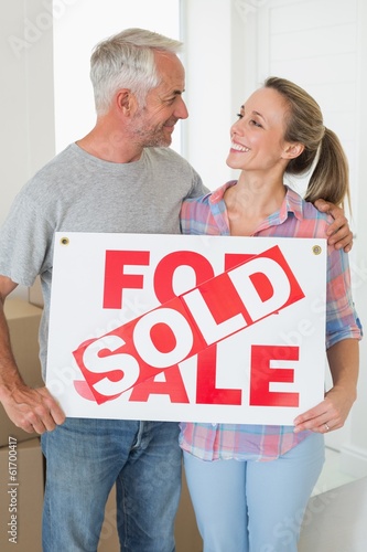 Photo: Happy couple standing and holding sold sign Happy couple standing and holding sold sign