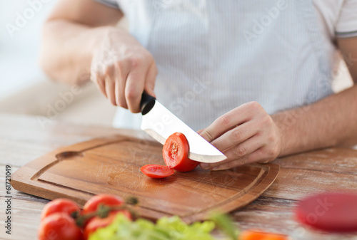 Photo: male hand cutting tomato on board with knife male hand cutting tomato on board with knife