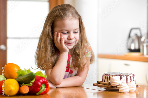 Photo: kid choosing between healthy vegetables and tasty sweets kid choosing between healthy vegetables and tasty sweets