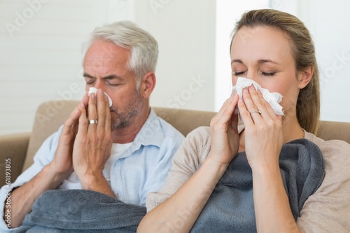 Photo: Sick couple blowing their noses sitting on the couch Sick couple blowing their noses sitting on the couch