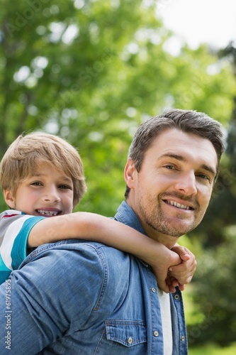 Photo: Portrait of a father carrying young boy on back Portrait of a father carrying young boy on back