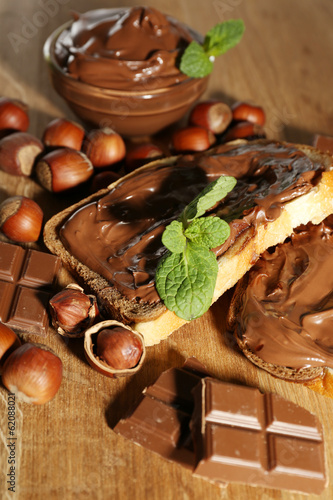 Photo: Bread with sweet chocolate hazelnut spread on wooden background Bread with sweet chocolate hazelnut spread on wooden background