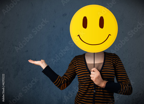 Photo: Young woman holding a smiley face emoticon Young woman holding a smiley face emoticon