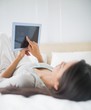 Young girl lying on bed looking up at her tablet pc Young girl lying on bed looking up at her tablet pc